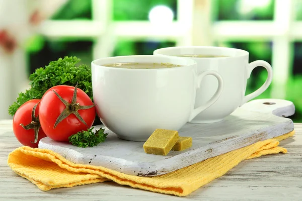 Kopjes soep met bouillonblokjes op houten tafel — Stockfoto