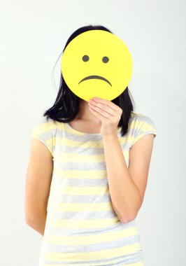 gri arka plan üzerinde üzgün smiley ile kağıt tutan genç kadın