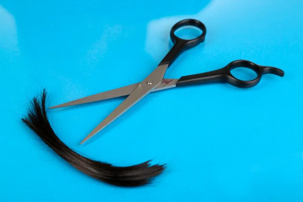 Pedaços de cabelo cortados com tesoura em fundo azul — Fotografia de Stock