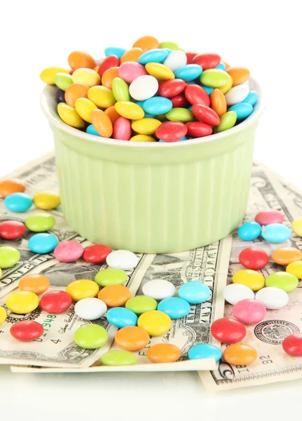 Cuenco con caramelos de colores de pie en billetes de dólar aislados en blanco — Foto de Stock