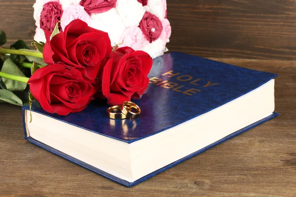 Wedding rings on bible with roses on wooden background — Stock Photo, Image