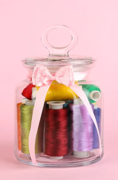 Glass jar containing various colored thread on pink background — Stock Photo, Image