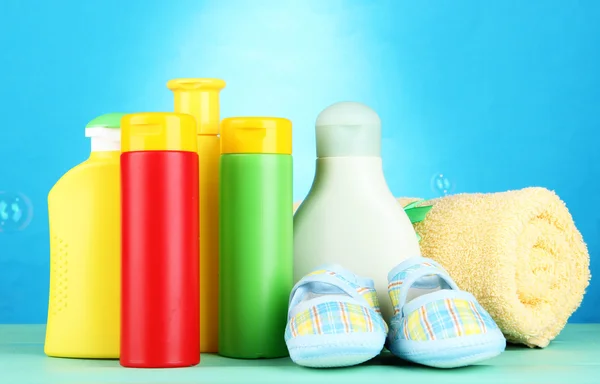 Baby cosmetics, towel and boots on wooden table, on blue background — Stock Photo, Image