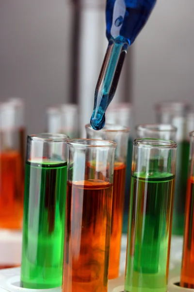Laboratorní pipety s kapkou barvy kapaliny přes skleněné zkumavky, zblízka — Stock fotografie