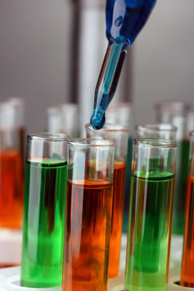 Pipeta de laboratório com gota de líquido de cor sobre tubos de ensaio de vidro, de perto — Fotografia de Stock