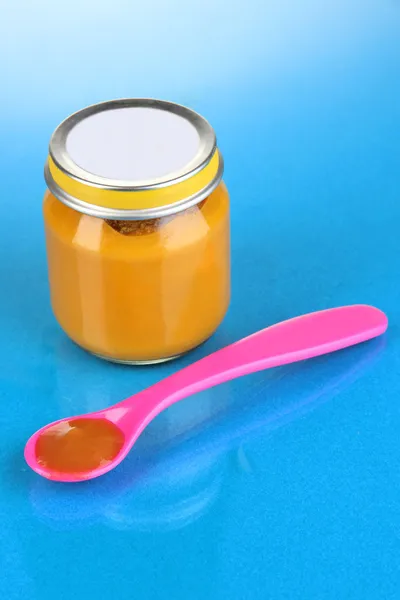 Color spoon for baby food with baby nutrition on blue background — Stock Photo, Image