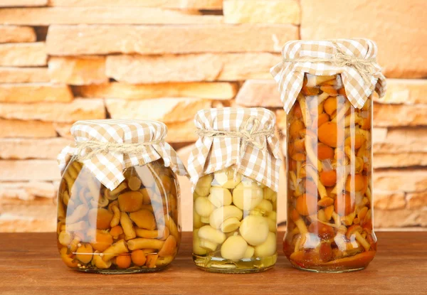 Delicious marinated mushrooms in glass jars, on wooden table on bright background — Stock Photo, Image