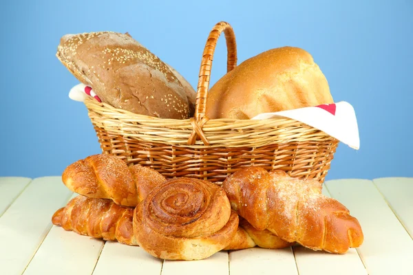 Composition avec pain et rouleaux, dans un panier en osier sur une table en bois, sur fond de couleur — Photo