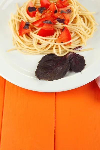 Спагетти с помидорами и листьями базилика на деревянном фоне — стоковое фото