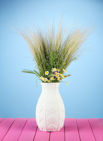 Bouquet of wild flowers and herbs, in vase, on wooden table on color background