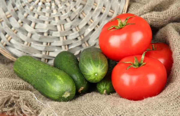 Läckra gröna gurkor och röda tomater på säckväv bakgrund — Stockfoto