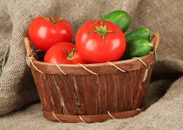 Tasty green cucumbers and red tomatoes in basket, on sackcloth background — Stock Photo, Image