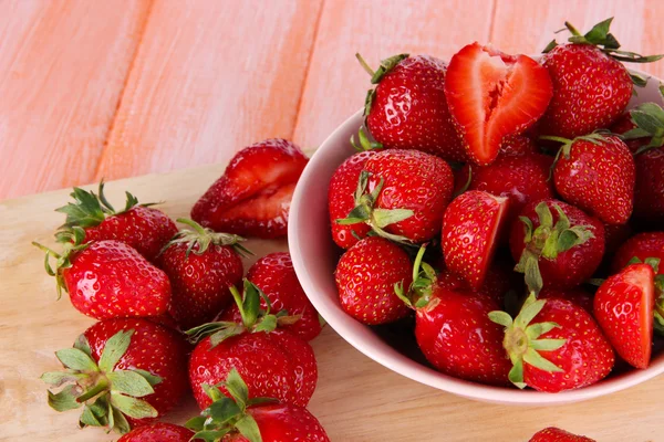 Strawberries in bowl on cutting board on wooden table — Stock Photo, Image