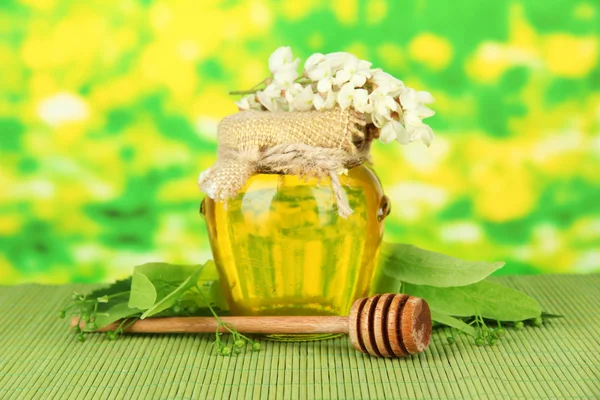 Tarro de miel con flores de lima, acacia sobre estera de bambú de color sobre fondo brillante — Foto de Stock