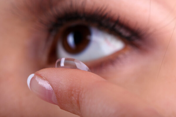 Young woman putting contact lens in her eye close up