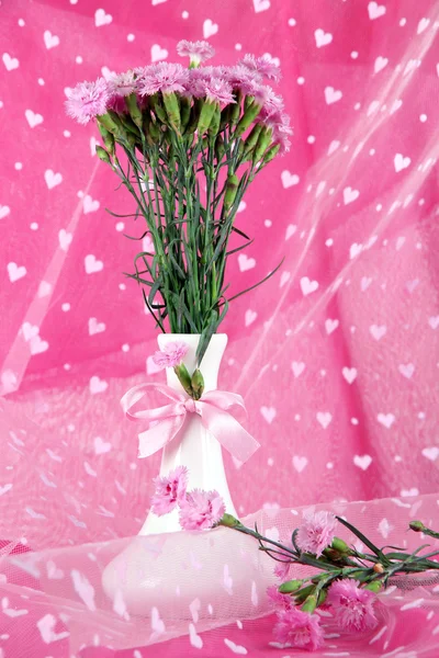 Mnoho malých pink hřebíček v váza na pozadí světle růžové látky — Stock fotografie