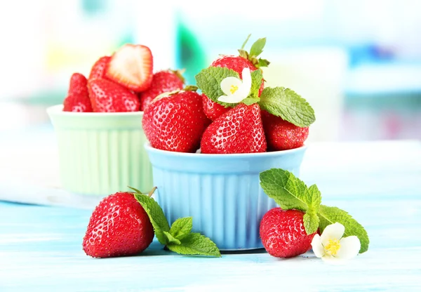 Ripe sweet strawberries in bowls on blue wooden table — Stock Photo, Image