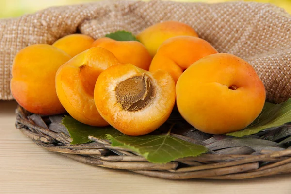 Apricots on wicker coasters on wooden table on nature background — Stock Photo, Image