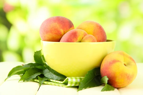 Спелые сладкие персики на деревянном столе в миске, на открытом воздухе — стоковое фото