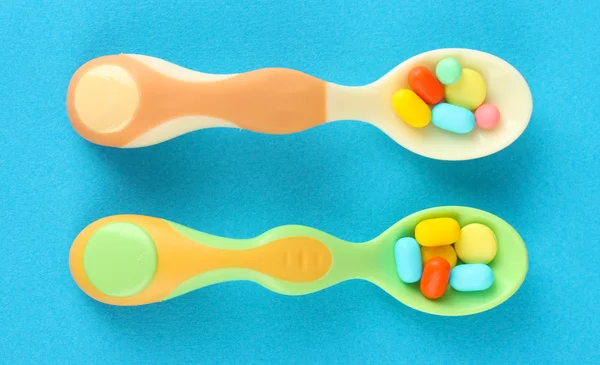 Plastic spoons with color pills on blue background — Stock Photo, Image