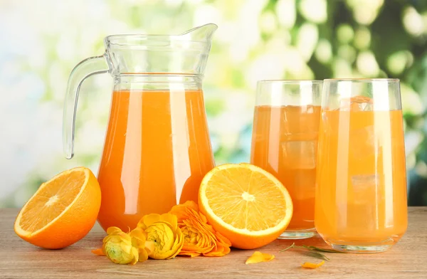 Glasögon och tillbringare med apelsinjuice på träbord, på grön bakgrund — Stockfoto