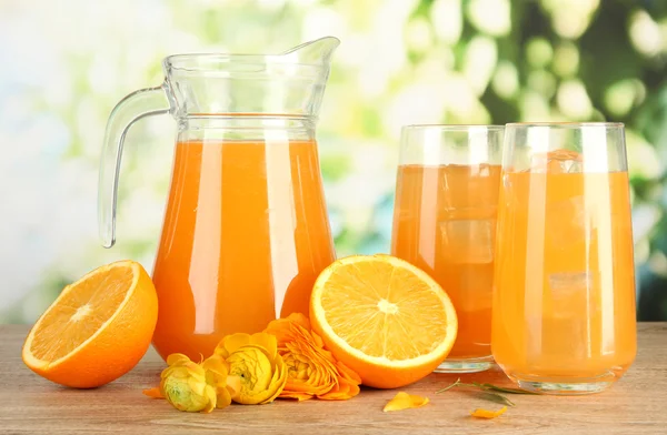 Copos e jarro de suco de laranja na mesa de madeira, no fundo verde — Fotografia de Stock