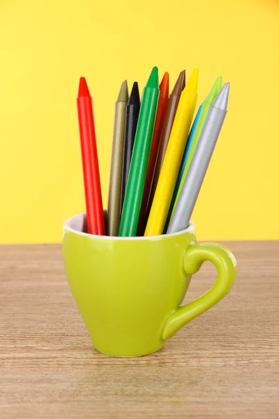 Barevné tužky v poháru na stole na žlutém podkladu — Stock fotografie