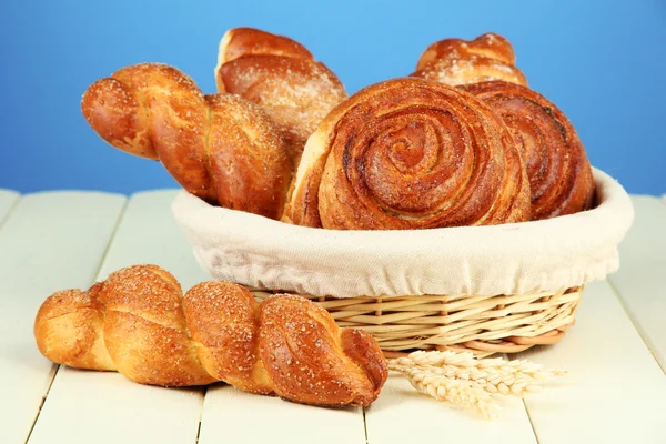 Samenstelling met broodjes in rieten mand, op houten tafel, op een achtergrond met kleur — Stockfoto