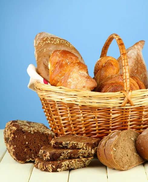 Σύνθεση με ψωμί και ψωμάκια, στο ψάθινο καλάθι στο ξύλινο τραπέζι, σε φόντο χρώμα — Φωτογραφία Αρχείου