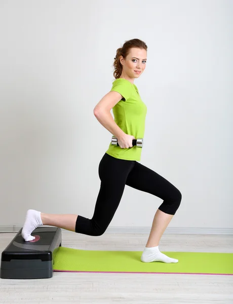 Beautiful young woman exercises with dumbbell on stepper — Stock Photo, Image