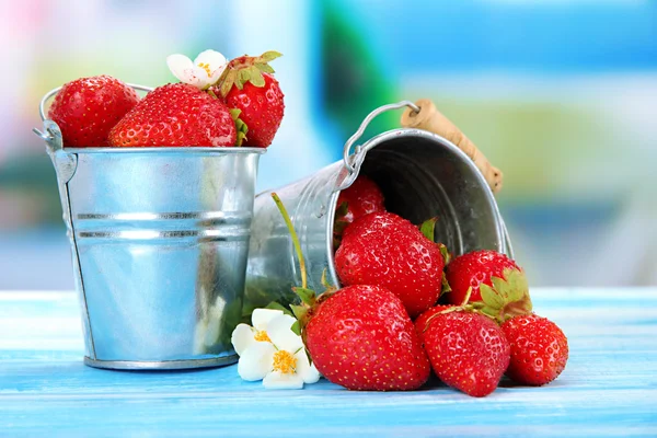 Reife süße Erdbeeren in Metalleimern auf blauem Holztisch — Stockfoto