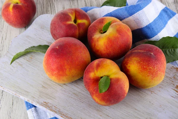 Peaches on board on napkin on table on wooden background — Stock Photo, Image