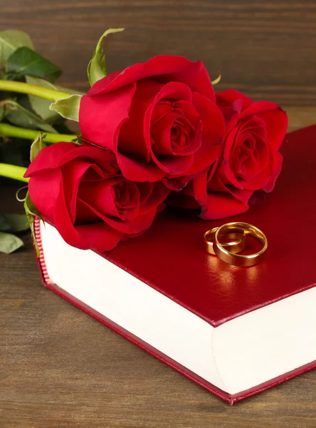 Wedding rings on bible with roses on wooden background — Stock Photo, Image