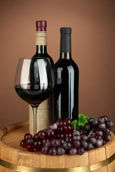 Composition of wine bottle, glass of red wine, grape on wooden barrel, on color background — Stock Photo, Image