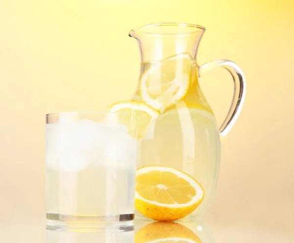 Lemonade in pitcher and glass on yellow background — Stock Photo, Image