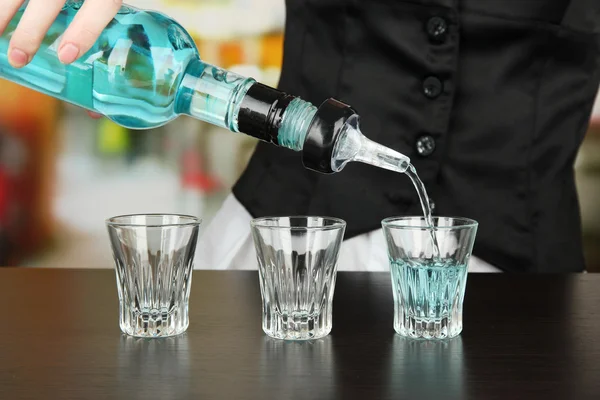 Barmen hand with bottle pouring beverage into glasses, on bright background — Stock Photo, Image