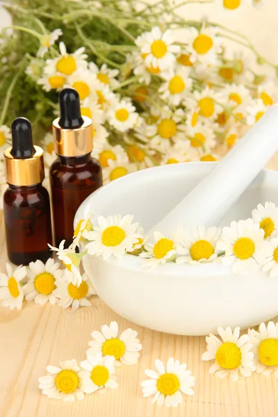 Essential oil and chamomile flowers in mortar on wooden table — Stock Photo, Image