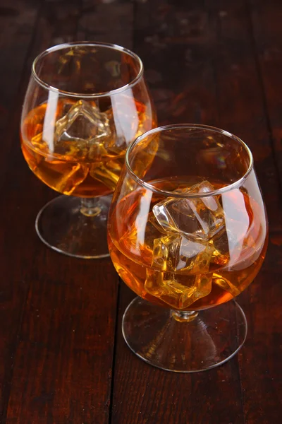 Brandy glasses with ice on wooden background — Stock Photo, Image