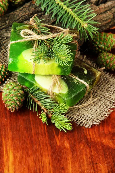 Jabón hecho a mano y conos de pino verde sobre mesa de madera — Foto de Stock