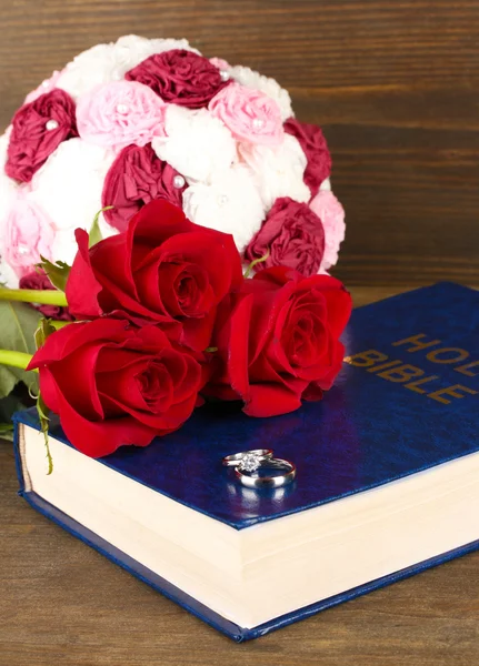 Wedding rings on bible with roses on wooden background — Stock Photo, Image