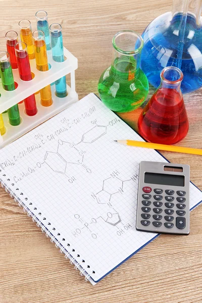 Test tubes with colorful liquids and formulas on table — Stock Photo, Image