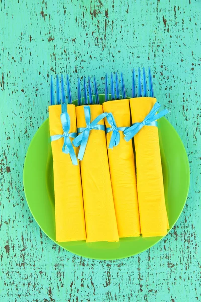 Garfos de plástico azul envolto em guardanapos de papel amarelo, na cor de fundo de madeira — Fotografia de Stock