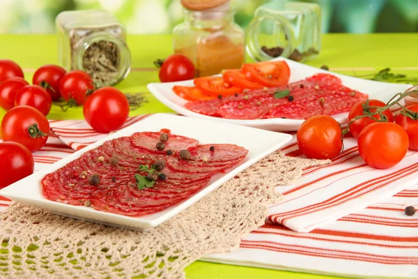 Tasty salami on plates on wooden table on natural background — Stock Photo, Image