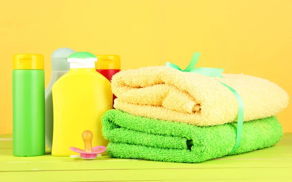 Cosméticos e toalhas de bebê na mesa de madeira, no fundo amarelo — Fotografia de Stock