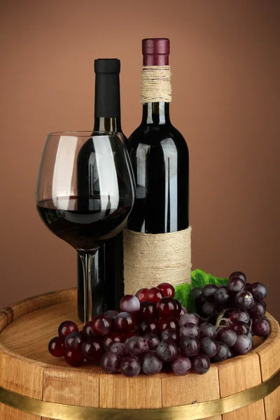 ワインのボトル、赤ワインのガラス、色の背景上の木製の樽にブドウの組成 — ストック写真