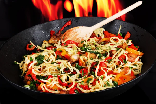 Noodles with vegetables on wok on fire background — Stock Photo, Image