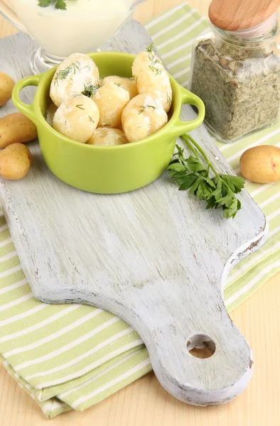 Jeunes pommes de terre tendres à la crème sure et aux herbes dans une casserole sur une planche de bois sur une table close-up — Photo