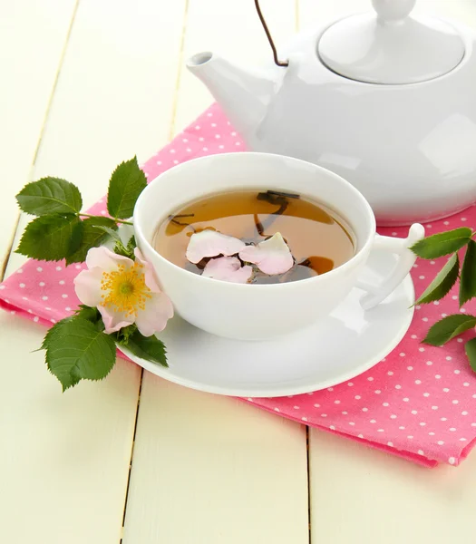 Xícara e bule de chá de ervas com flores de rosa do quadril na mesa de madeira branca — Fotografia de Stock