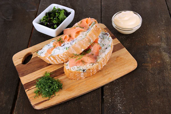 Sandwiches de pescado sobre tabla de cortar sobre mesa de madera — Foto de Stock