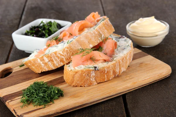 Sandwiches de pescado sobre tabla de cortar sobre mesa de madera — Foto de Stock